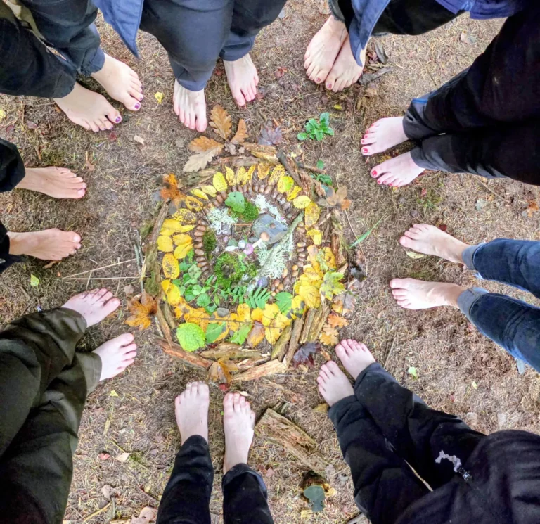 Personen stehen barfuß im Kreis, in der Mitte ein Bild aus Laub, Eicheln und Stöcken